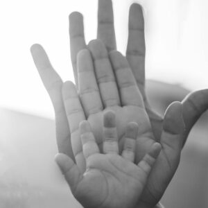 A child’s hand resting in the mother’s palm, both held by the father’s hand symbolizing ancestry, lineage, and family roots.