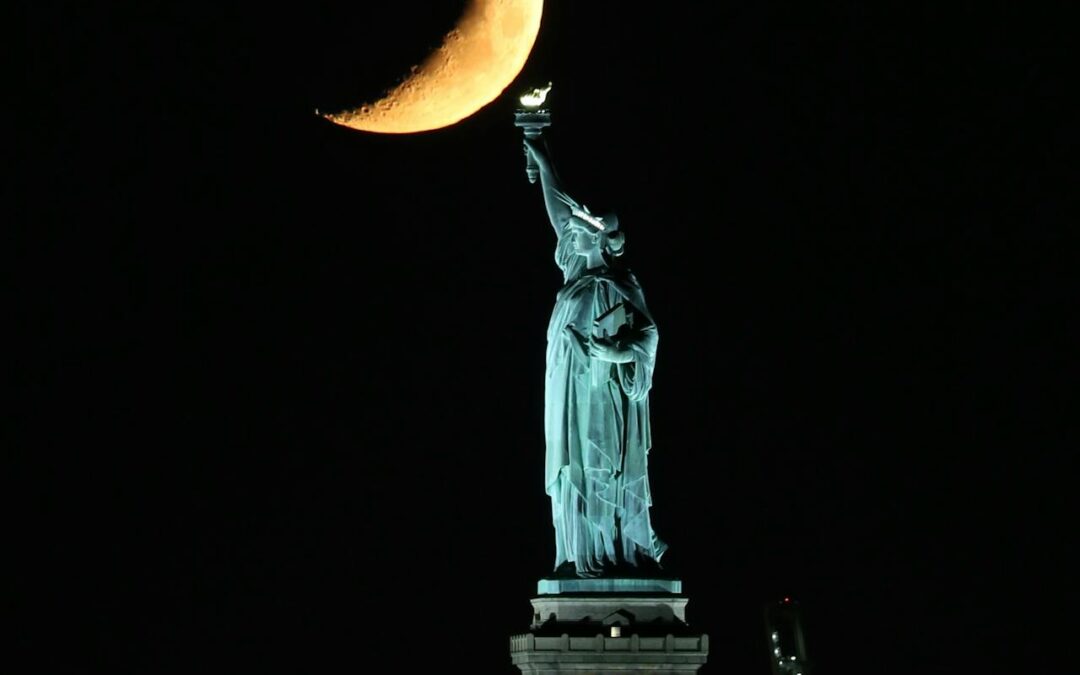 Crescent moon rising over the Statue of Liberty symbolizing the New Moon in Sagittarius and its themes of freedom, vision, and expansion.