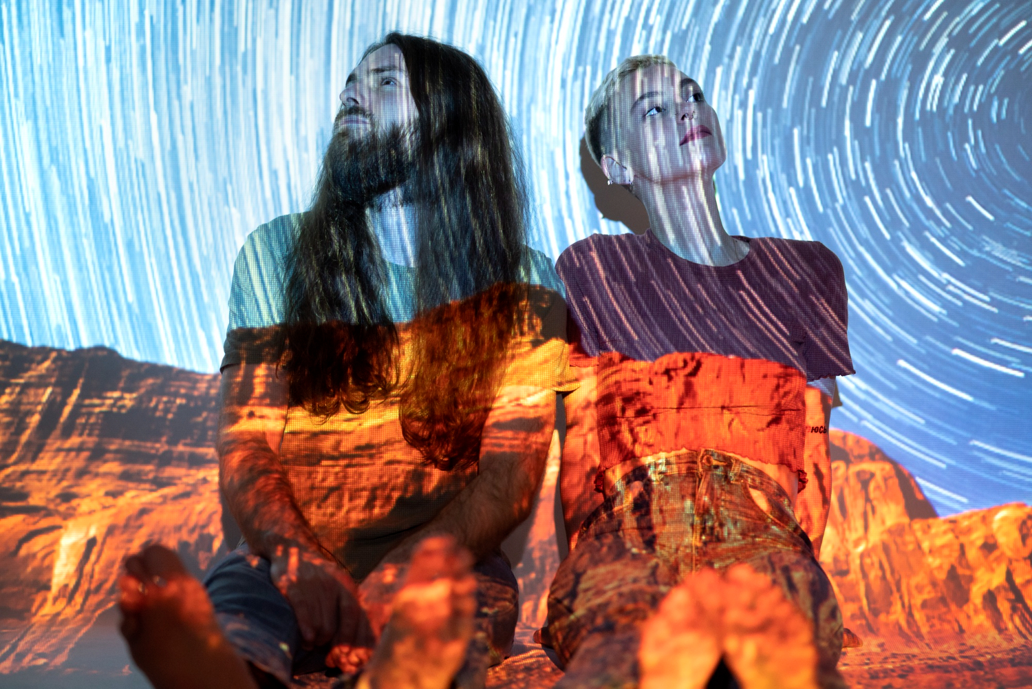 Couple sitting on the floor with a projector casting a starry universe pattern over them.
