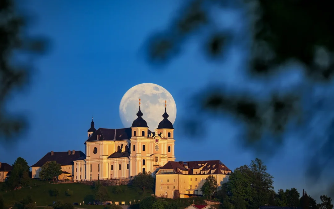 Stunning view of a Baroque church silhouetted against a large blue full moon in the night sky.